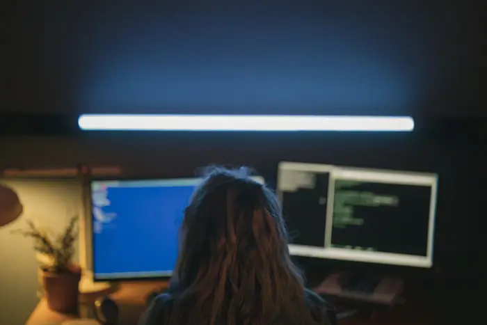 Pessoa programando à noite diante de dois monitores com código